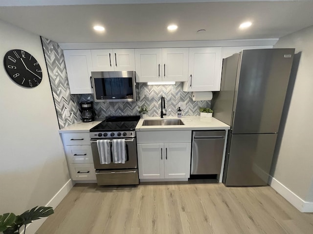 kitchen featuring baseboards, appliances with stainless steel finishes, light wood-style flooring, and a sink