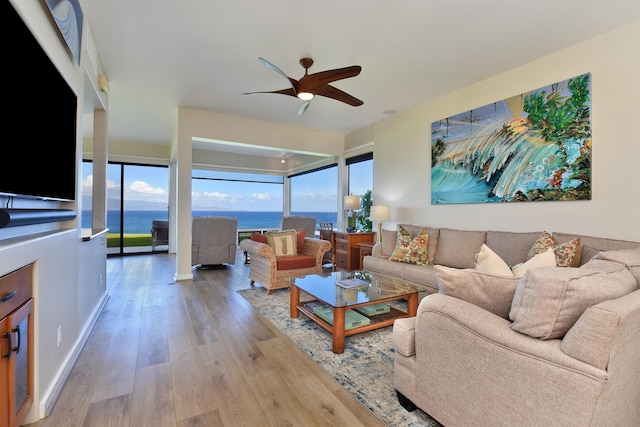 living room with light wood-type flooring, ceiling fan, and a water view