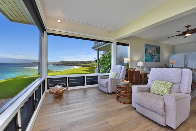 sunroom / solarium with ceiling fan, track lighting, and a water view