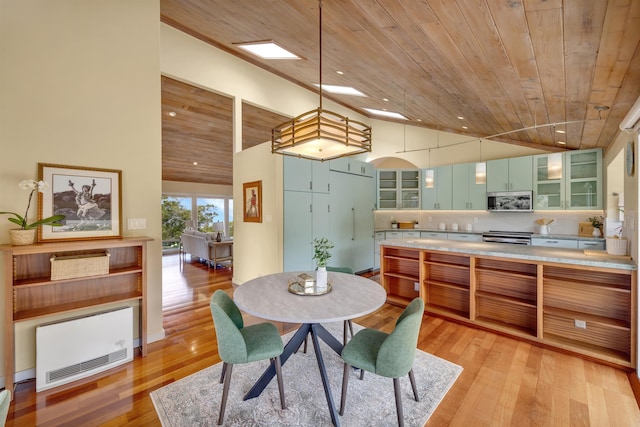 kitchen with glass insert cabinets, stainless steel microwave, light countertops, pendant lighting, and green cabinetry