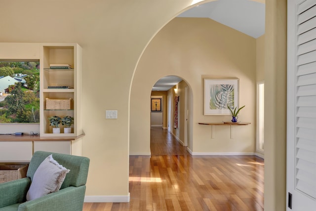 hallway with light wood-type flooring, arched walkways, high vaulted ceiling, and baseboards