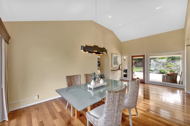 dining area featuring high vaulted ceiling, light wood-type flooring, and baseboards