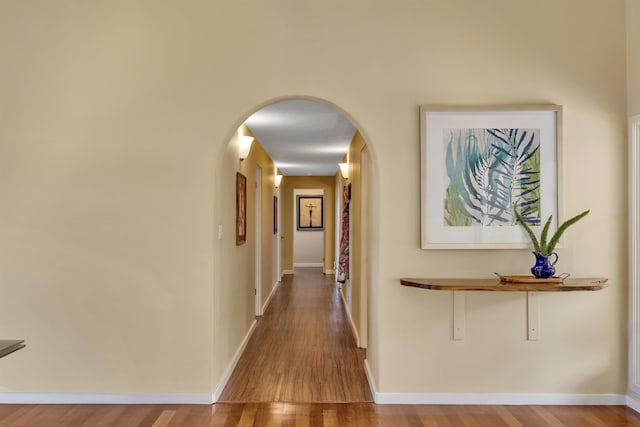 corridor featuring baseboards, arched walkways, and wood finished floors