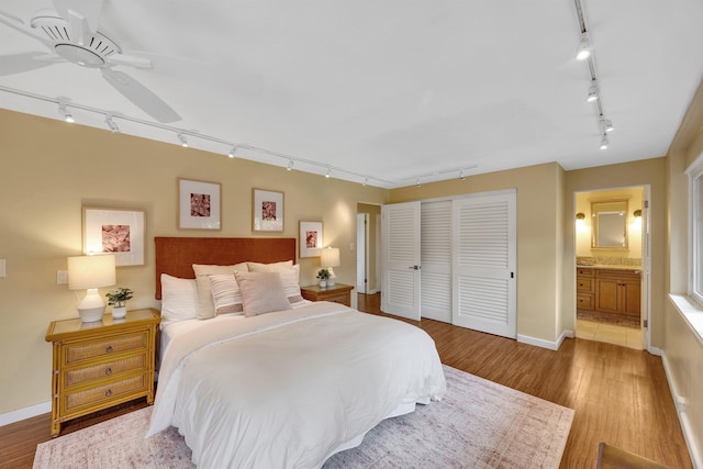 bedroom featuring light wood finished floors, a closet, connected bathroom, track lighting, and baseboards