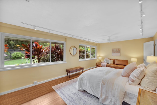 bedroom with rail lighting, baseboards, and wood finished floors