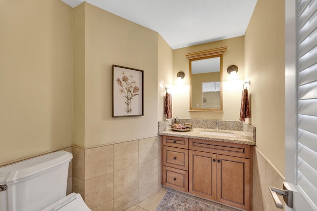 half bath featuring tile patterned flooring, wainscoting, tile walls, and toilet