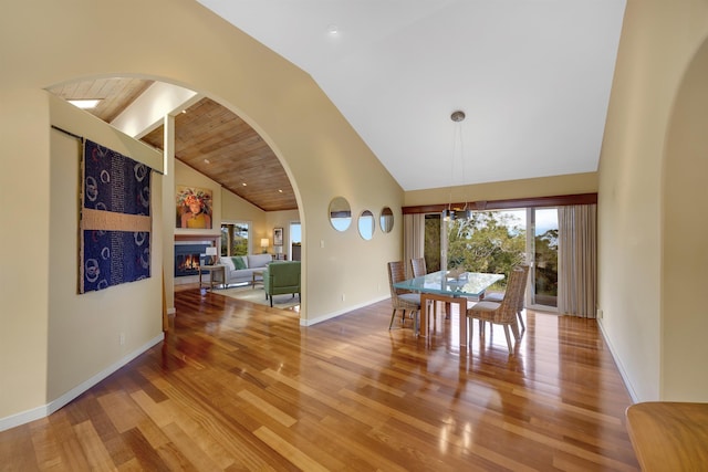 dining space with high vaulted ceiling, wood finished floors, baseboards, beamed ceiling, and a glass covered fireplace