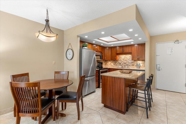 kitchen with light stone counters, stainless steel appliances, a tray ceiling, a kitchen island, and hanging light fixtures