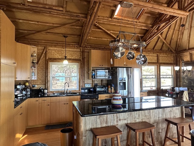kitchen with a breakfast bar, a sink, dark countertops, light brown cabinets, and appliances with stainless steel finishes