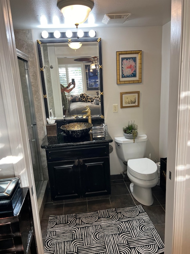 bathroom featuring ceiling fan, vanity, a shower with shower door, tile patterned floors, and toilet