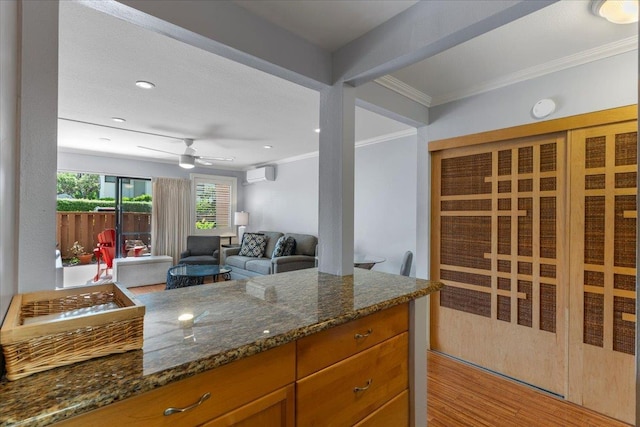 kitchen with light wood-type flooring, ornamental molding, dark stone counters, ceiling fan, and an AC wall unit