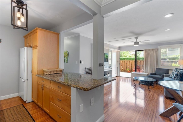 kitchen with kitchen peninsula, ceiling fan, light hardwood / wood-style flooring, dark stone countertops, and white fridge
