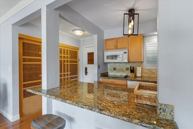 kitchen featuring kitchen peninsula, dark stone counters, pendant lighting, light hardwood / wood-style floors, and decorative backsplash