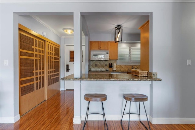 kitchen with decorative backsplash, dark stone counters, decorative light fixtures, and wood-type flooring