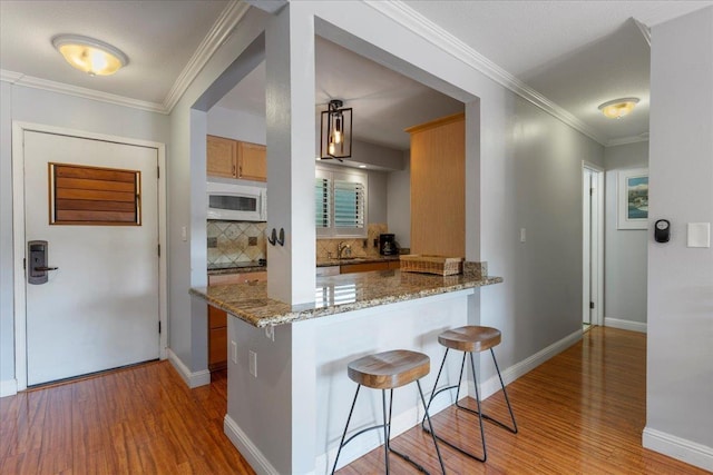 kitchen featuring light hardwood / wood-style flooring, decorative backsplash, light stone countertops, kitchen peninsula, and a breakfast bar area