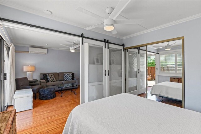 bedroom with a wall mounted air conditioner, ceiling fan, crown molding, a barn door, and hardwood / wood-style flooring