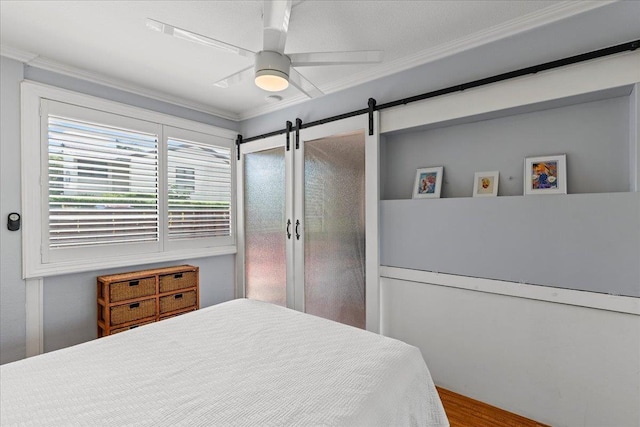 bedroom with a barn door, ceiling fan, wood-type flooring, and ornamental molding