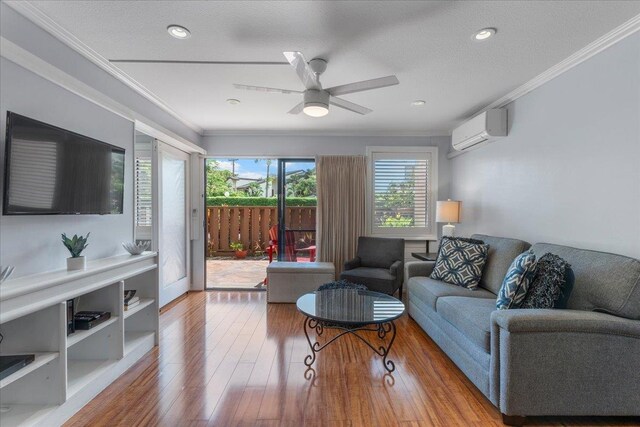living room featuring hardwood / wood-style flooring, ceiling fan, ornamental molding, a textured ceiling, and a wall unit AC