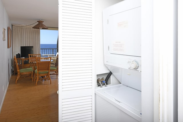 washroom with hardwood / wood-style floors and stacked washing maching and dryer