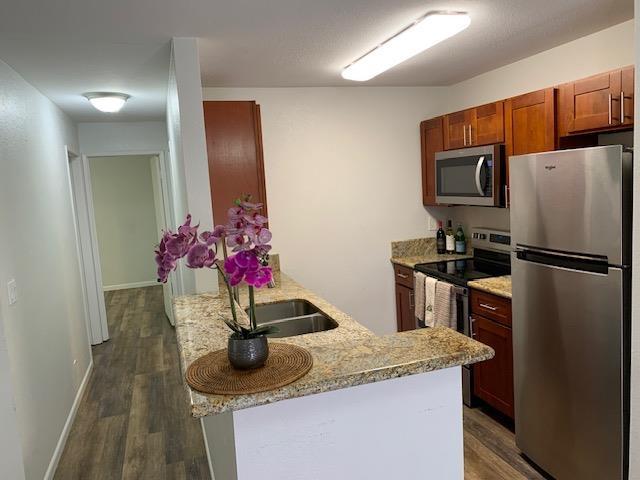 kitchen with sink, stainless steel appliances, light stone counters, dark hardwood / wood-style flooring, and kitchen peninsula