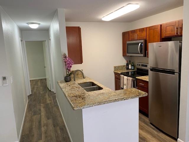 kitchen with sink, stainless steel appliances, light stone counters, dark hardwood / wood-style flooring, and kitchen peninsula