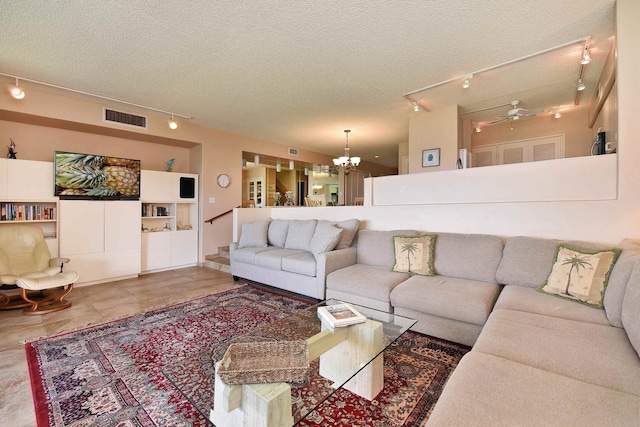 living room featuring light tile floors, ceiling fan with notable chandelier, a textured ceiling, built in shelves, and rail lighting