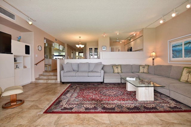 tiled living room with track lighting, a textured ceiling, ceiling fan with notable chandelier, and built in shelves