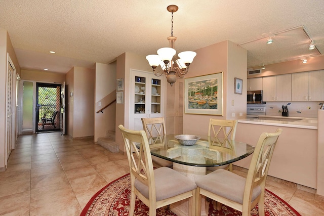 dining room with a textured ceiling, light tile floors, a notable chandelier, and rail lighting