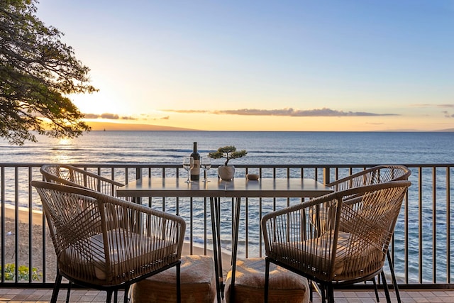 balcony at dusk featuring a beach view and a water view