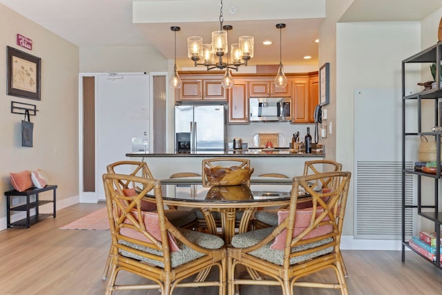 kitchen featuring kitchen peninsula, appliances with stainless steel finishes, pendant lighting, an inviting chandelier, and light hardwood / wood-style floors