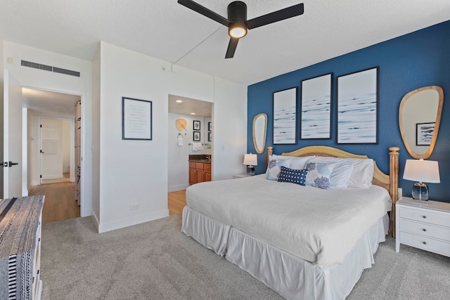 bedroom with a textured ceiling, ceiling fan, light colored carpet, and ensuite bathroom