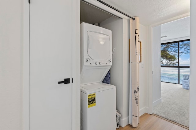 laundry area with stacked washer and dryer, a water view, light hardwood / wood-style floors, and a textured ceiling