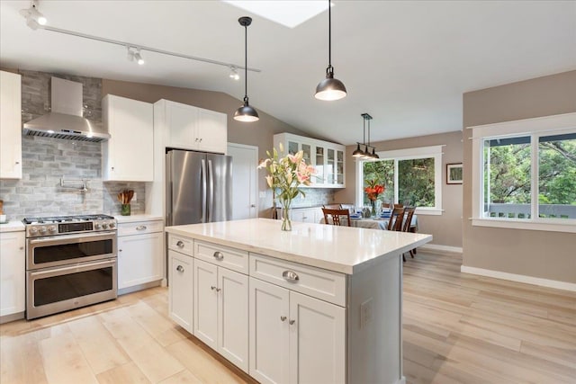 kitchen featuring appliances with stainless steel finishes, wall chimney exhaust hood, white cabinets, track lighting, and pendant lighting