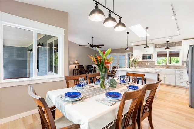 dining area featuring a skylight, ceiling fan, sink, light hardwood / wood-style floors, and track lighting