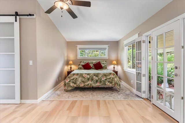 bedroom featuring lofted ceiling, ceiling fan, light wood-type flooring, and a barn door