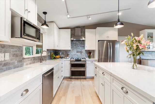 kitchen featuring appliances with stainless steel finishes, hanging light fixtures, track lighting, tasteful backsplash, and wall chimney range hood