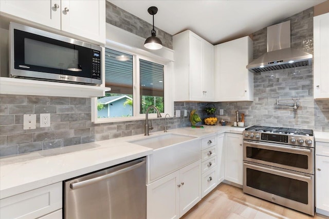 kitchen featuring decorative light fixtures, backsplash, stainless steel appliances, wall chimney exhaust hood, and white cabinetry