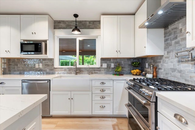 kitchen featuring pendant lighting, wall chimney range hood, backsplash, and stainless steel appliances