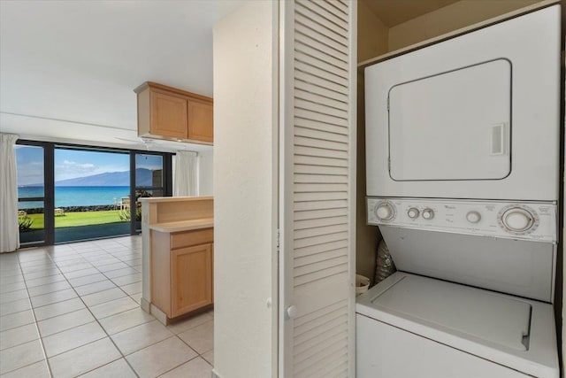 laundry area with a water view, stacked washer / dryer, and light tile patterned floors