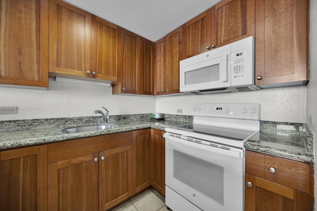 kitchen featuring white appliances, a sink, brown cabinets, and stone countertops