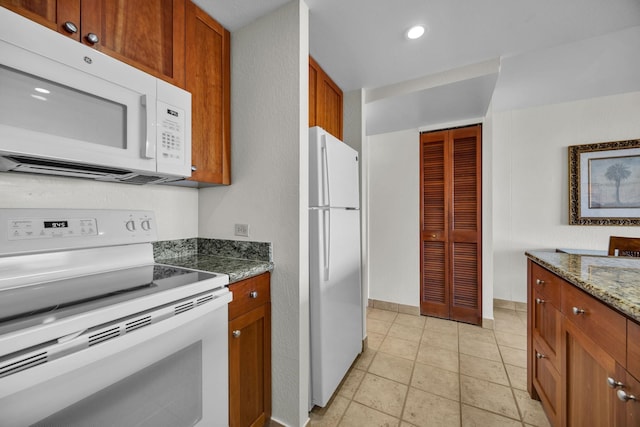 kitchen featuring white appliances, brown cabinetry, dark stone countertops, recessed lighting, and light tile patterned flooring