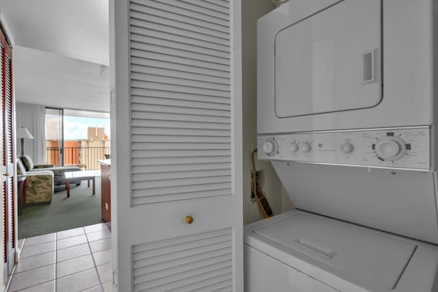 clothes washing area featuring stacked washer and clothes dryer, light tile patterned floors, and light carpet