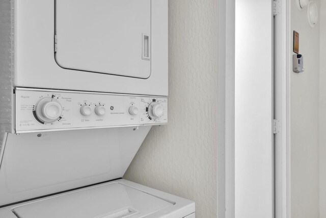 washroom featuring stacked washer / drying machine and a textured wall