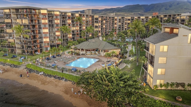 aerial view at dusk of view of pool, a view of apartment building / complex, and a mountain view