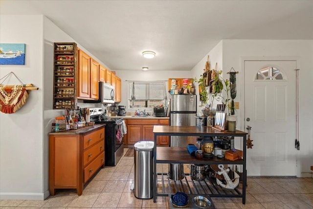 kitchen with appliances with stainless steel finishes, light tile patterned flooring, a sink, and baseboards