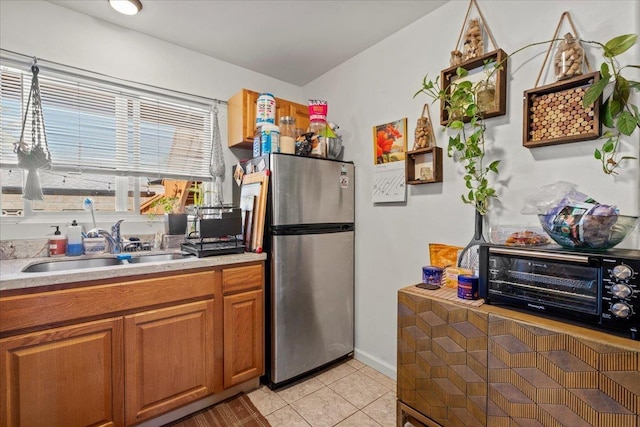 kitchen featuring light tile patterned floors, a sink, light countertops, freestanding refrigerator, and brown cabinets