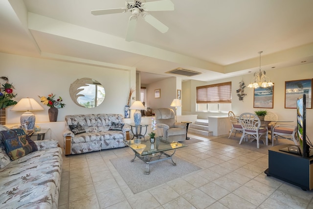 tiled living room with a raised ceiling and ceiling fan with notable chandelier