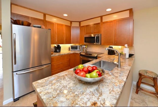 kitchen featuring sink, tasteful backsplash, light stone counters, kitchen peninsula, and stainless steel appliances