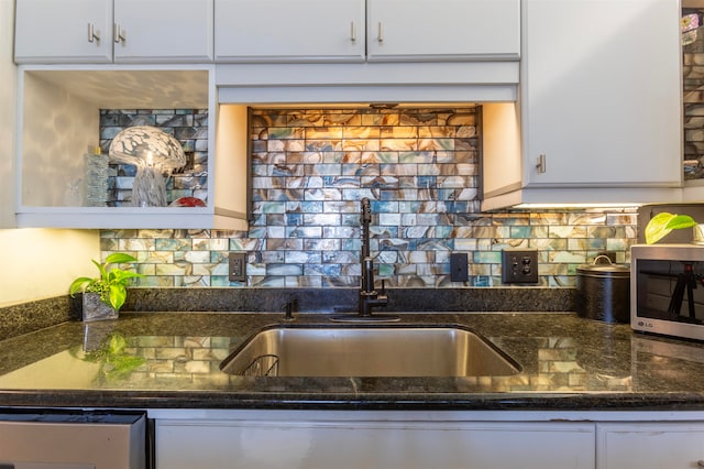 kitchen with dark stone countertops, a sink, white cabinetry, appliances with stainless steel finishes, and decorative backsplash