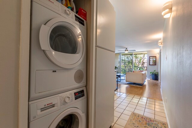 clothes washing area with a ceiling fan, laundry area, stacked washing maching and dryer, and light tile patterned floors